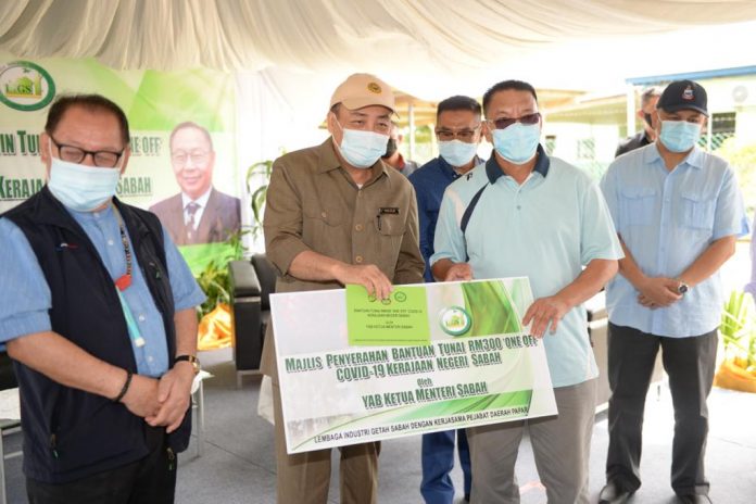 Ketua Menteri Datuk Seri Hajiji Noor menyampaikan bantuan tunai one-off Rm300 kepada salah seorang peneroka kecil ladang getah di Kampung Kabang, Papar, hari ini.